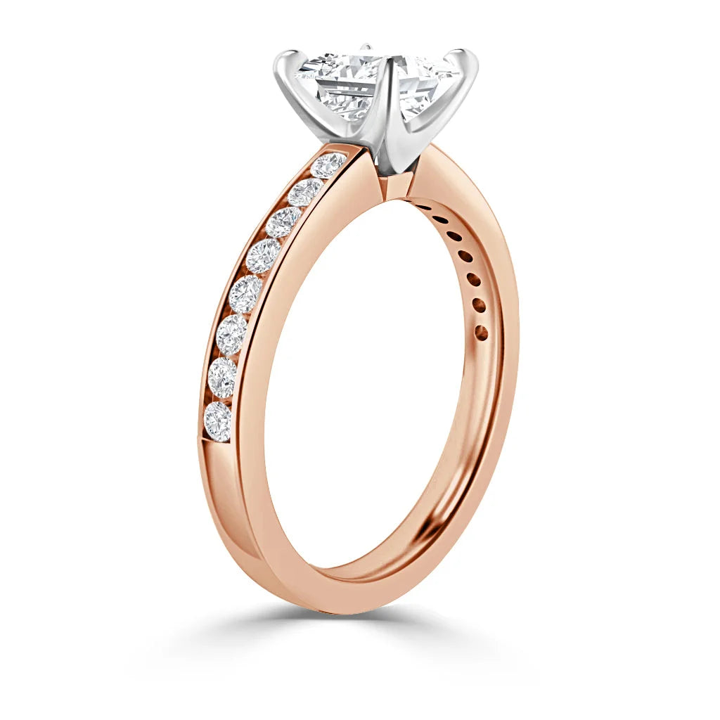 A rose gold ring with a round diamond solitaire and side stones set along the band, white gold prongs.