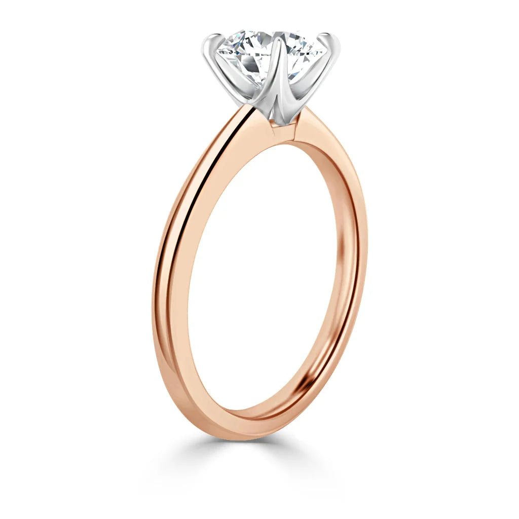 Rose gold engagement ring with a round diamond solitaire in a white gold prong setting, viewed from the side.