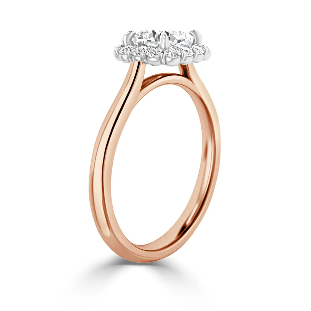 Rose gold ring with a split band and a round diamond halo setting, viewed from the side on a white background.