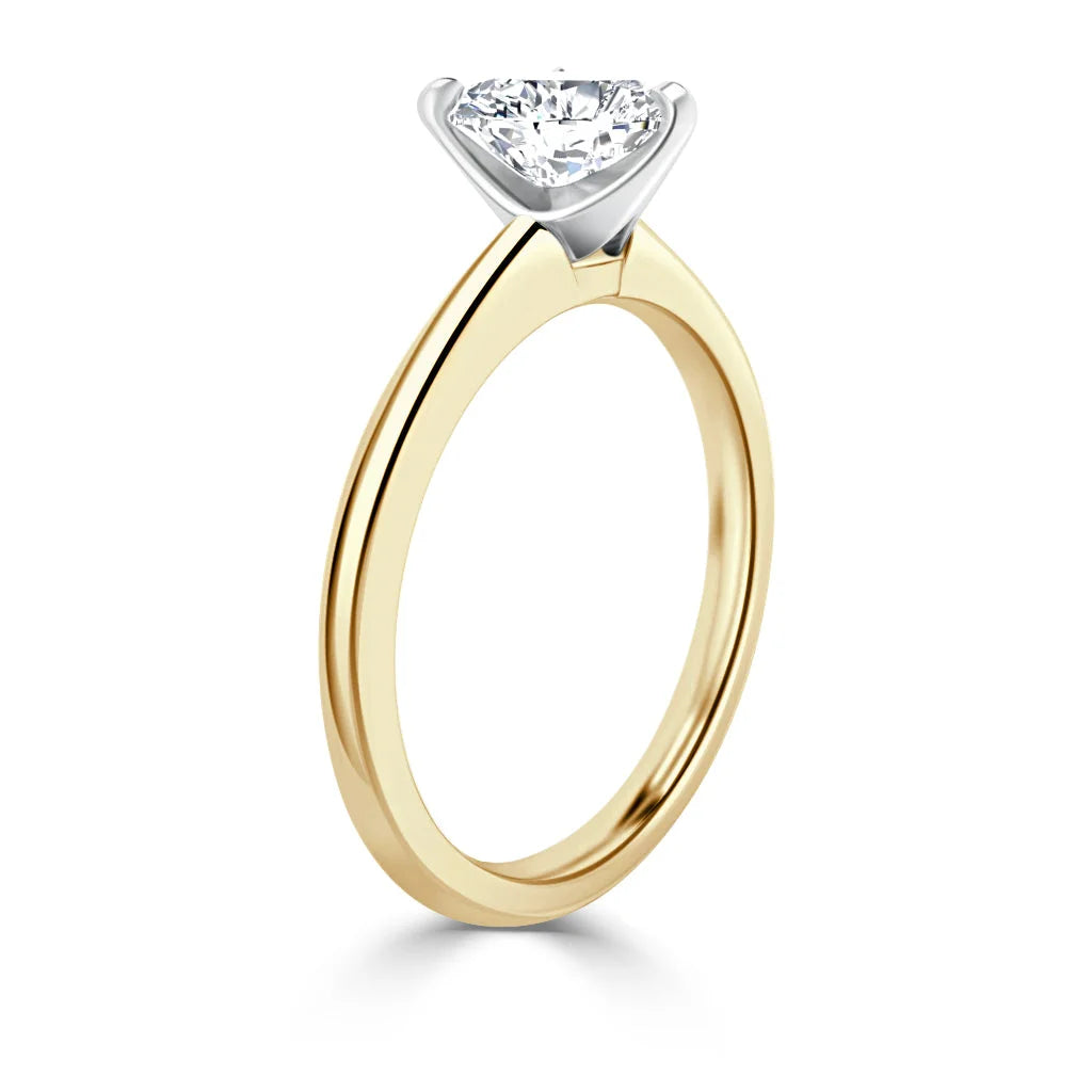 A gold solitaire ring with a round diamond set in a white metal prong setting, viewed from the side.