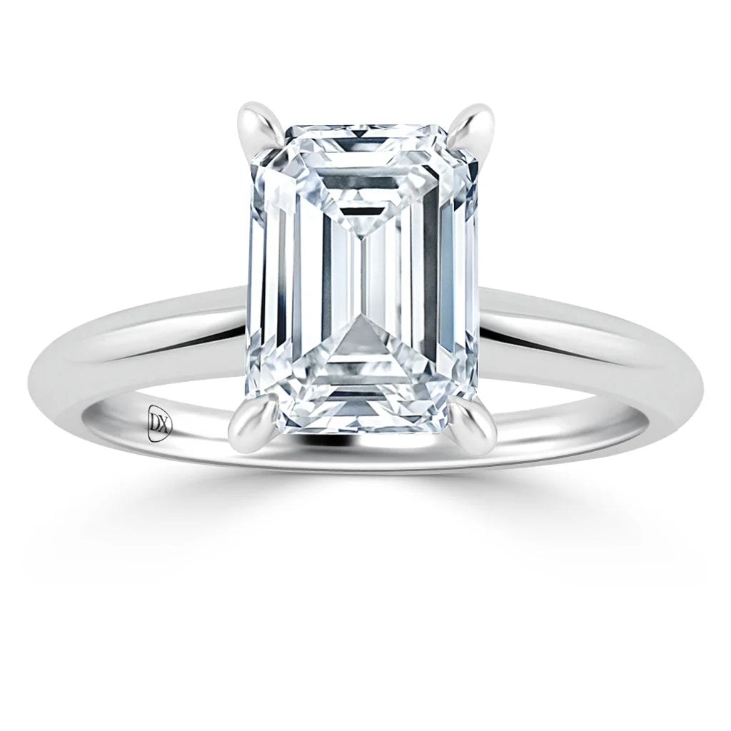 A silver ring with an emerald-cut clear diamond solitaire set in four prongs on a plain band.
