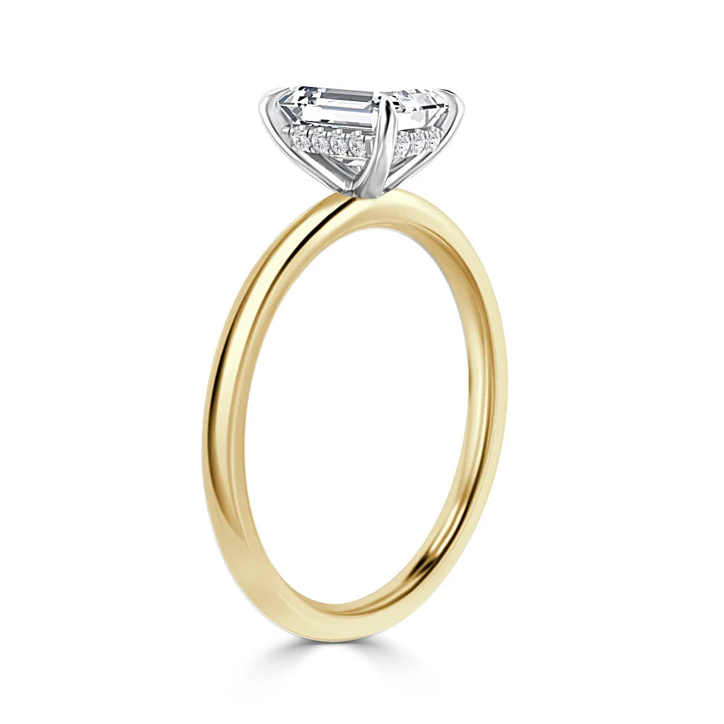 A gold ring with a large emerald-cut diamond set in a white gold prong setting, viewed from the side.