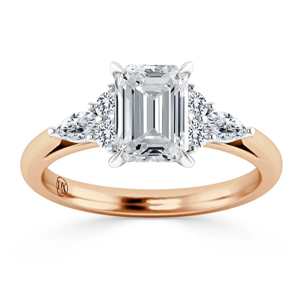 A rose gold ring with an emerald-cut diamond center, flanked by three round side diamonds on each side.