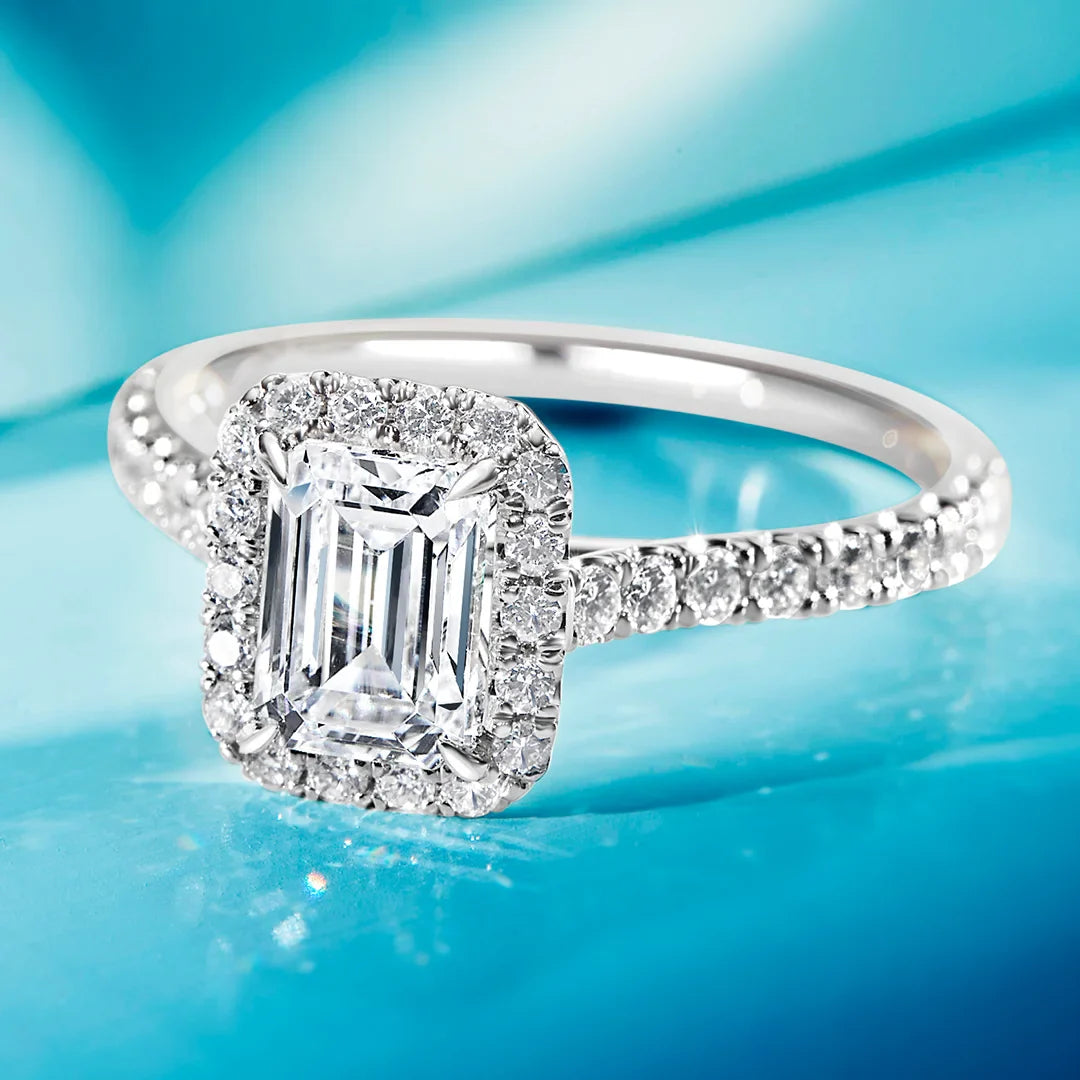 A diamond ring with an emerald-cut center stone and a halo of smaller diamonds on a blue background.
