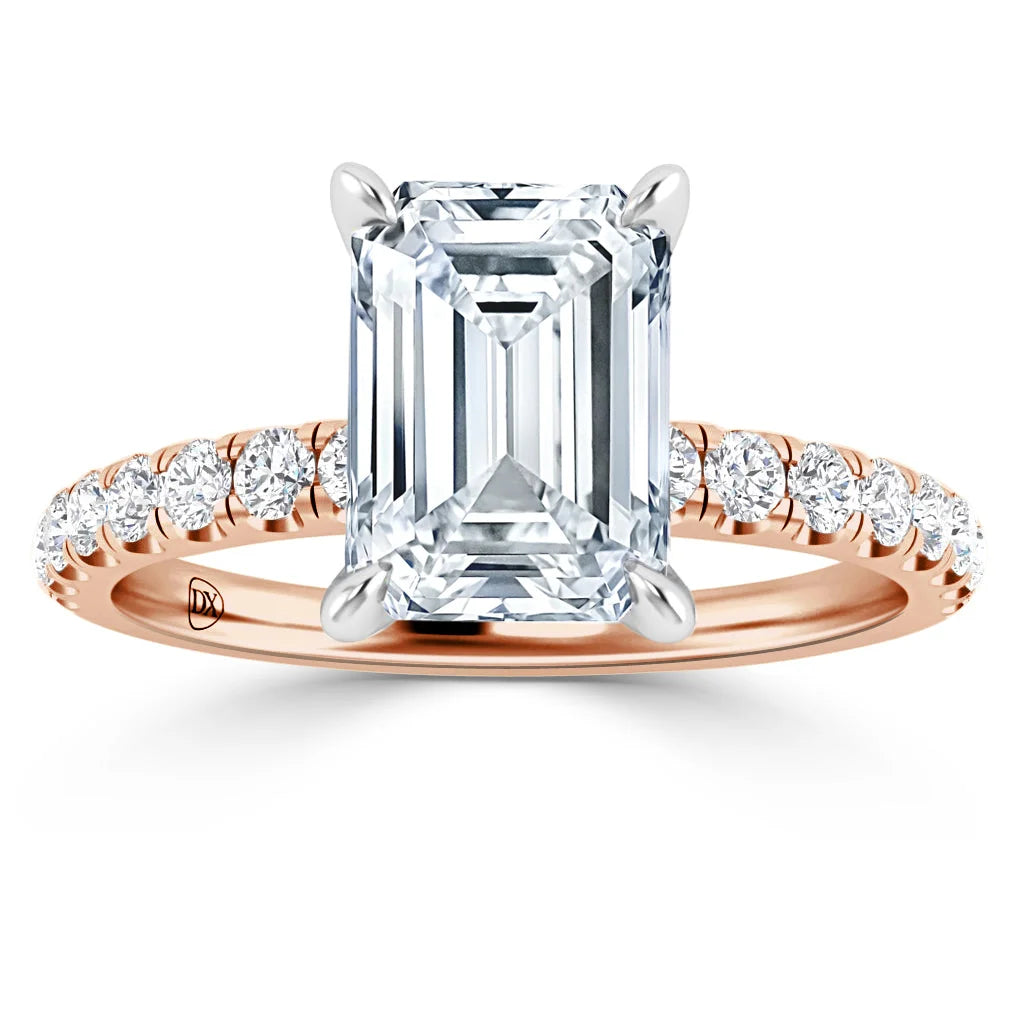Emerald-cut diamond ring with rose gold band and round diamonds set along the band, on white background.