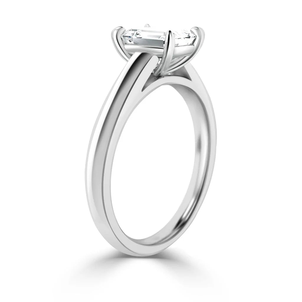 A silver solitaire engagement ring with a prong-set rectangular diamond on a smooth, polished band.