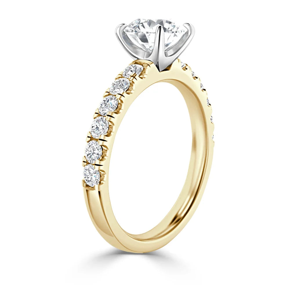 A yellow gold engagement ring with a round solitaire diamond and a band set with smaller round diamonds.
