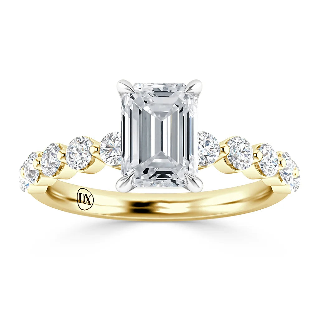 Gold ring with emerald-cut center diamond and round diamonds set along the band, engraved with “DX” inside.