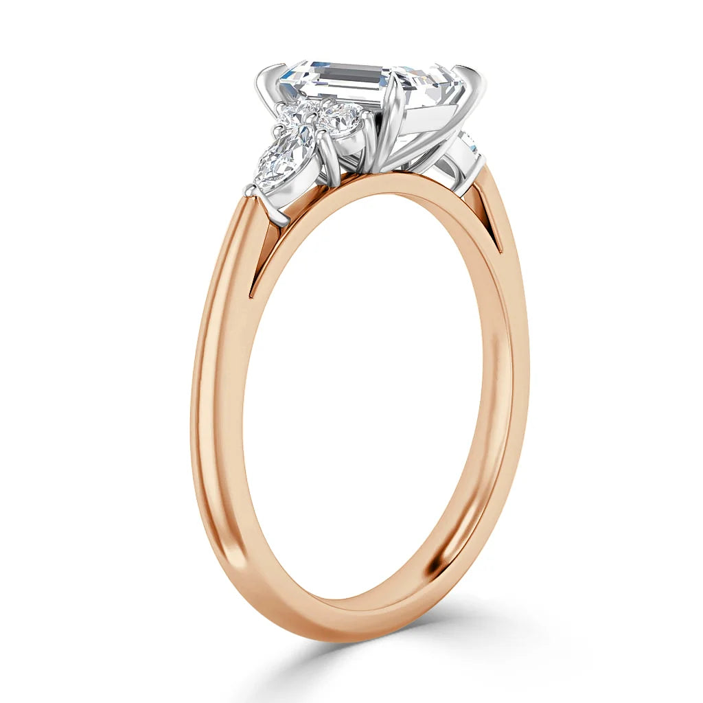 A rose gold ring with a large emerald-cut center diamond and two marquise side diamonds in a white gold setting.