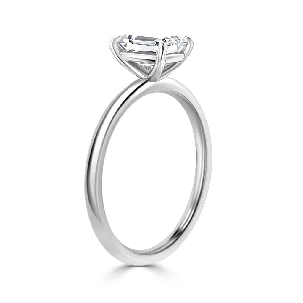 A solitaire emerald-cut diamond ring with a thin, polished platinum band shown on a white background.