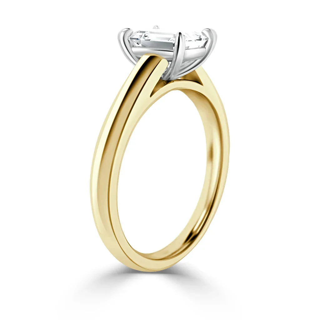 Yellow gold ring with a raised white gold prong setting holding a single rectangular emerald-cut diamond.