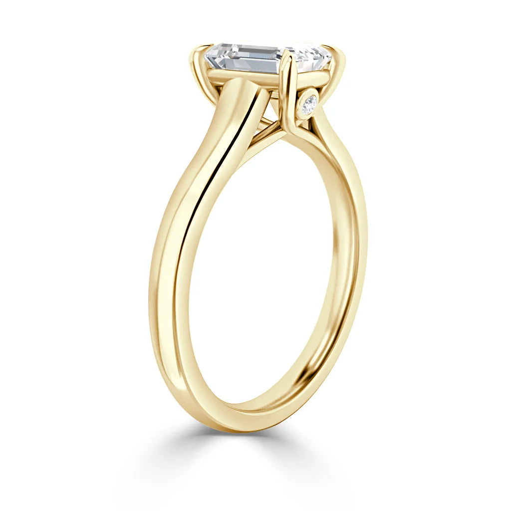 Yellow gold ring with a solitaire emerald-cut diamond in a prong setting, shown from a side angle.