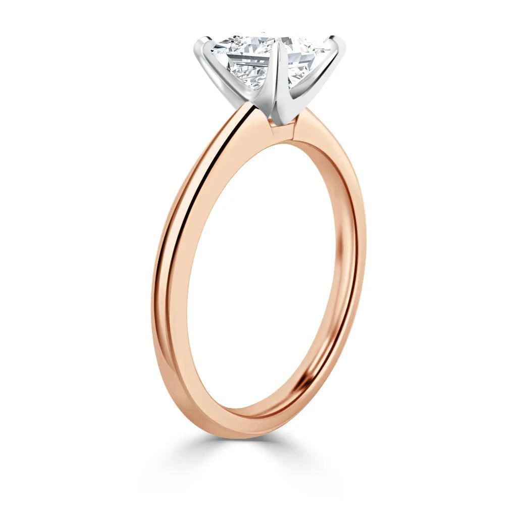 A solitaire diamond ring with a rose gold band and a white gold prong setting, shown from the side.