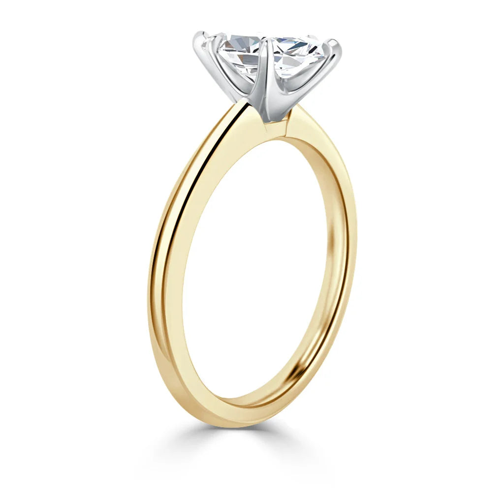 A gold ring with a round solitaire diamond held by a white gold prong setting, shown from the side.