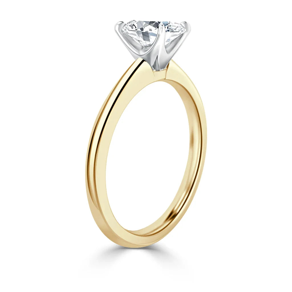 A gold solitaire ring with a round diamond set in a white gold prong setting, shown from the side.