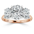 A rose gold ring with three large oval-cut diamonds, the center stone flanked by two slightly smaller diamonds.