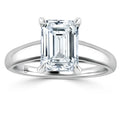 Emerald-cut diamond solitaire ring with a plain, polished white metal band on a white background.