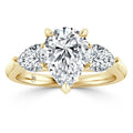 A gold ring with a large pear-shaped diamond center and two smaller round diamonds on each side.