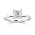 A solitaire ring with an emerald-cut diamond set on a thin, plain white gold band against a white background.