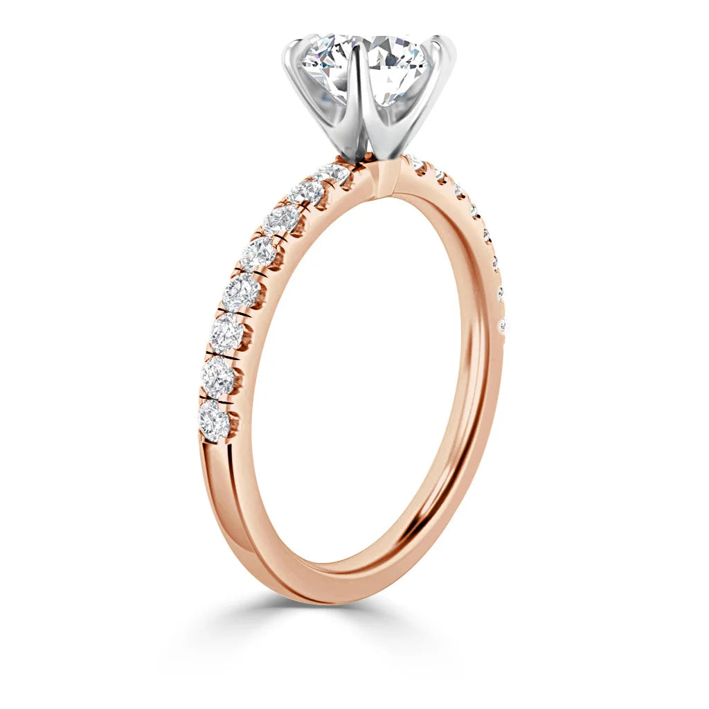A rose gold ring with a row of diamonds on the band and a large round solitaire diamond in a silver prong setting.