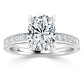 Oval diamond ring with prong setting; band features channel-set smaller diamonds on a white metal band.