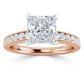A rose gold ring with a large princess-cut diamond and smaller diamonds on the band.