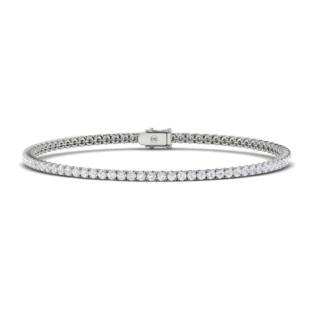 A delicate silver tennis bracelet with a single row of round white diamonds and a secure clasp, on a white background.