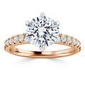 A rose gold ring with a large round diamond center stone and smaller diamonds on the band, on a white background.