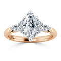 A marquise-cut diamond ring with side stones set on a rose gold band, displayed on a white background.
