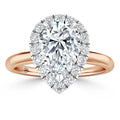 A pear-shaped diamond ring with a halo of smaller diamonds on a rose gold band, shown on a white background.