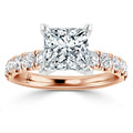 Rose gold ring with a large princess-cut diamond and smaller round diamonds along the band, white background.