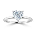A heart-shaped diamond solitaire ring set on a simple, polished white gold band against a white background.