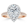 A pear-shaped diamond ring with a halo of smaller diamonds on a rose gold band, set with pavé diamonds.