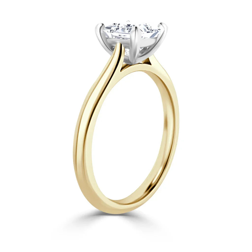 A gold solitaire ring with a round diamond held by a white gold four-prong setting, shown from the side.