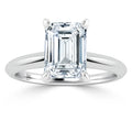 A silver ring with an emerald-cut clear diamond solitaire set in four prongs on a plain band.