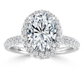 Oval diamond ring with a halo of smaller diamonds on a diamond-encrusted band, set in white metal.
