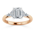 A rose gold ring with an emerald-cut diamond center, flanked by three round side diamonds on each side.