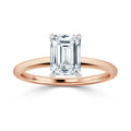 A rose gold ring with an emerald-cut diamond solitaire set in a four-prong white gold setting.