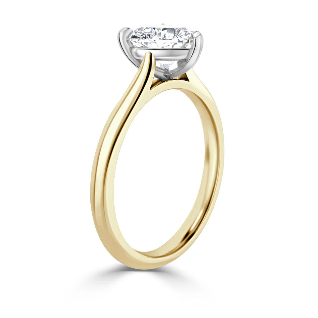 A solitaire diamond ring with a yellow gold band and a white gold prong setting holding the round diamond.