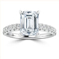 Emerald-cut diamond ring with a band set with smaller round diamonds on a polished metal setting.