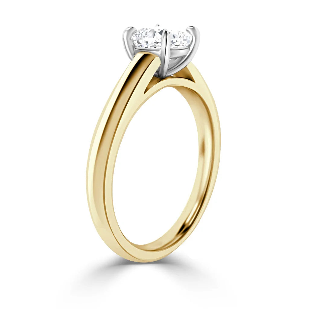 A gold engagement ring with a solitaire round diamond set in a white prong setting against a white background.