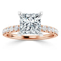 Rose gold ring with a large princess-cut diamond and pavé diamonds along the band, shown on a white background.