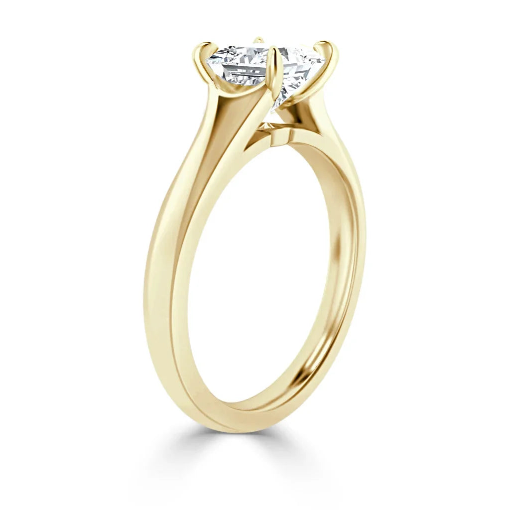 A gold solitaire ring with a round, prong-set diamond viewed from the side on a white background.