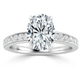 Oval-cut diamond ring with a diamond-studded band on a white gold or platinum setting, shown close up.