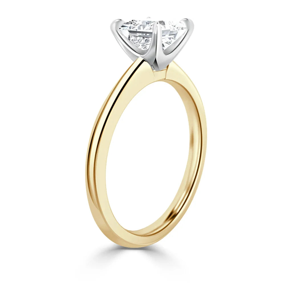 A gold solitaire ring with a round diamond in a white gold prong setting, viewed from the side.
