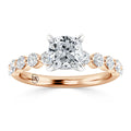 Rose gold ring with a cushion-cut center diamond and round diamonds on the band in a prong setting.
