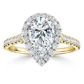 Pear-shaped diamond ring with a double halo and diamond-studded gold band, set against a white background.