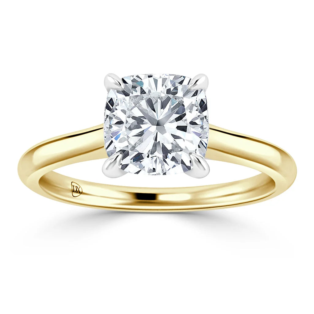 A gold band ring with a cushion-cut diamond solitaire set in four prongs on a white background.