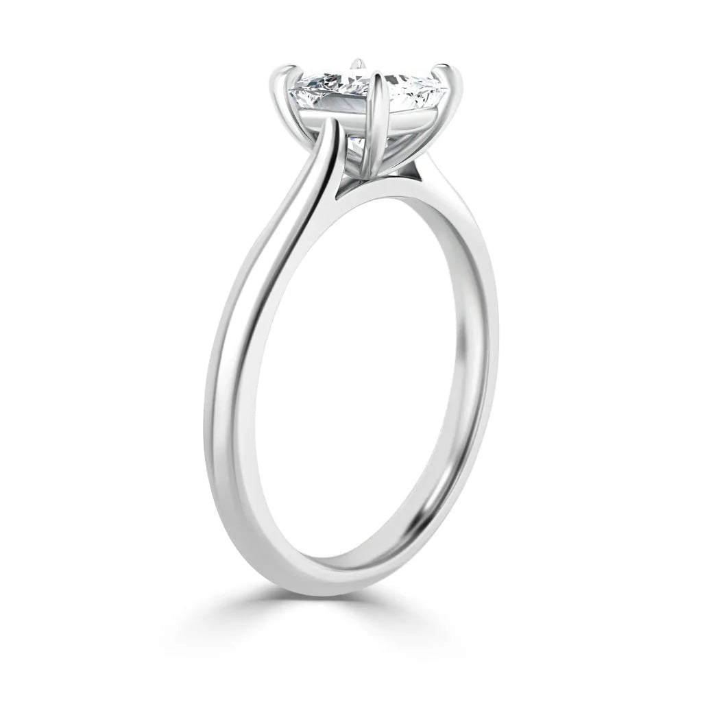 A silver solitaire engagement ring with a round diamond in a prong setting, shown from a side angle.