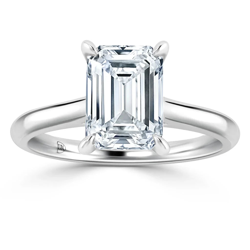 A solitaire emerald-cut diamond ring set on a simple platinum band against a white background.